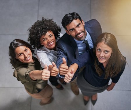 High angle portrait of a group of coworkers showing a thumbs up in the office.