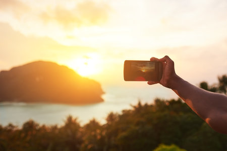 Every sunset is a poem without words. an unidentifiable tourist using a smartphone to photograph an island view.の写真素材