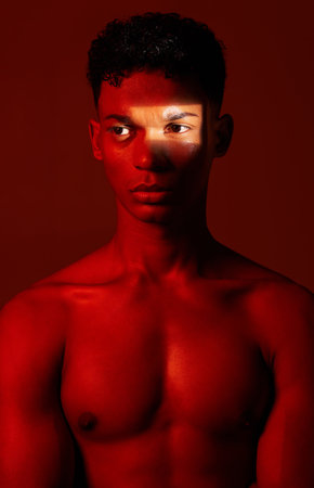 Beauty, red light and man in studio for health, wellness and skincare with a spotlight reflection. Body, self care and healthy male model from Mexico with cosmetics isolated by a red background.の写真素材
