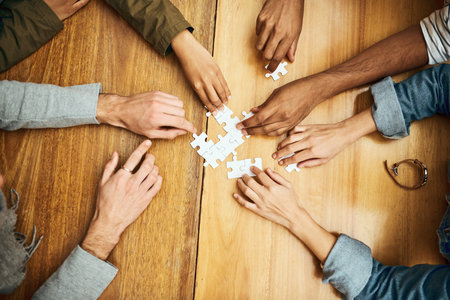 Teamwork gets the job done. High angle shot of a group of unrecognizable university students building a puzzle while studying in the library.の写真素材