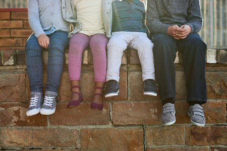 A group of unrecognizable elementary school kids sitting on a brick wall outside.の写真素材