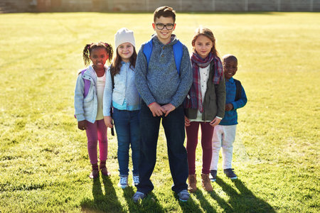 Portrait of a group of elementary school kids standing on the school lawn outside.