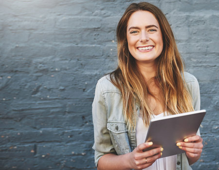 It keeps me connected and happy. Portrait of a young woman standing outdoors and using a digital...