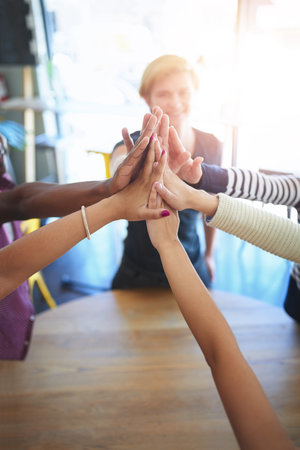 Live while youre young. a group of happy friends high fiving each other in a cafe.