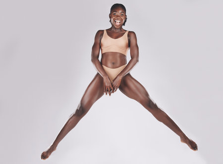 Fitness, jump and portrait of strong woman in underwear jumping on a studio background. Health, wellness and beauty of a healthy woman in lingerie in hop and feeling excited about exercise bodyの写真素材