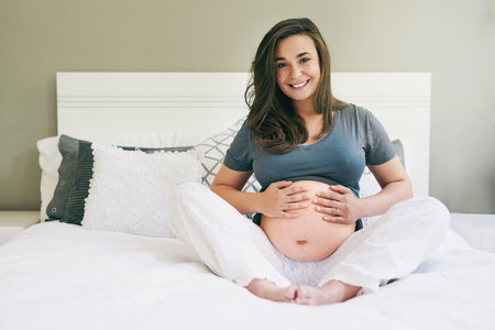 Want to feel him kick. a young pregnant woman relaxing at home.の写真素材