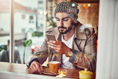 Catching up on some texts over coffee. a stylish young man reading a text message while sitting at a counter in a cafe.の写真素材