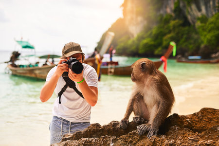 Make sure you get my good side. a young tourist taking a picture of a monkey while exploring a tropical beach.の写真素材