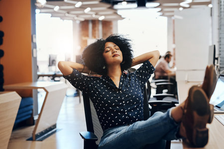 Just kick back and take a . minute. a relaxed looking young female designer lying back in her seat in the office during the day.の写真素材