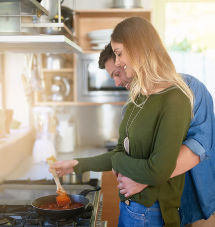 Their special ingredient is love. an affectionate young couple preparing dinner together at the stove in their kitchen.の写真素材