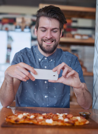 Straight to social media. a man taking a picture of his food at a restaurant.の写真素材
