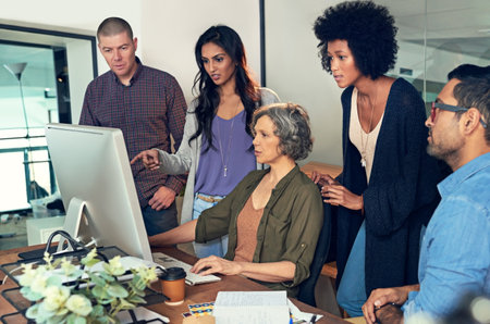 Its important to share critique and criticism as a team. a group of businesspeople discussing something on a computer in an office.の写真素材