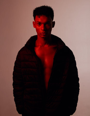 Portrait, fashion and style with a man model in studio on a wall background with red light for...