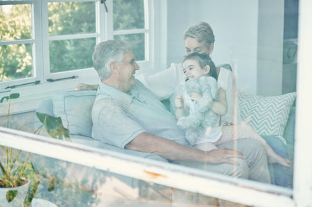 Family, girl with teddy bear and grandmother and grandfather in home, having fun and bonding. Support, care and love of happy grandparents playing with kid holding toy on sofa in house living room.の写真素材