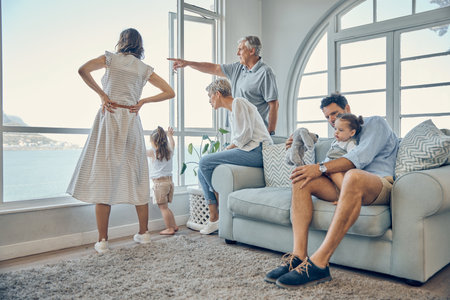 Travel, family and window in a living room of holiday house, bonding and relax while enjoying the view together. Vacation, home and happy family with kids, parents and grandparents and scenic viewの写真素材