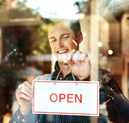 I finally followed my dreams. Closeup shot of a young man hanging up an open sign in a shop window.