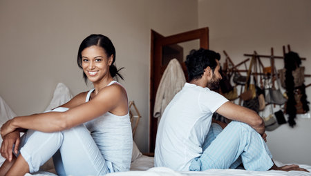 Time to get up and start our day. Portrait of a young woman sitting on a bed with her husband at home.の写真素材