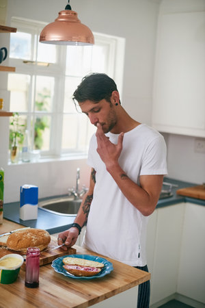 Thats a tasty sandwich. a handsome young man standing in his kitchen making a sandwich.の写真素材