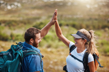 Couple, high five and hiking with motivation, goal and celebration for fitness target in nature with backpack. Man, woman and happy for partnership, excited or support while trekking together outdoorの写真素材
