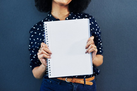 The start of a grand plan. Studio shot of a young woman holding up a blank notebook against a blue background.の写真素材