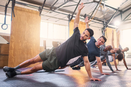 Strong man, personal trainer and group training with side plank exercise, workout and fitness in gym...