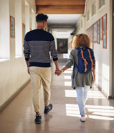 Walking her to class. Rearview shot of an affectionate young couple walking hand in hand through their university corridor.の写真素材