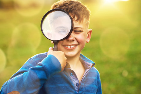 I spy with my little eye...Portrait of a cute little boy looking through a magnifying glass while standing outside.の写真素材
