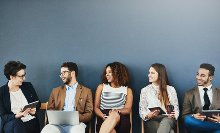 The job applicants are all getting along. Studio shot of a group of businesspeople using wireless technology and talking while waiting in line against a gray background.の写真素材
