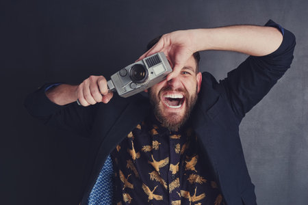 He has a special enthusiasm for film cameras. a trendy young man with a vintage camera posing against a dark background.の写真素材