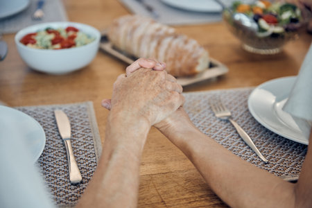 Family, food and prayer with senior couple holding hands, paying and gratitude at dining table for lunch, dinner and healthy diet. Man and woman saying grace, religion and grateful to pray and eatの写真素材