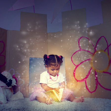 Her very first fairytale. an adorable little girl sitting on the floor and reading a glowing book.の写真素材