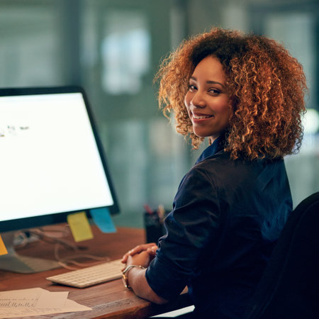 Stay positive, stay productive. Portrait of a happy young businesswoman using a computer during a late night at work.の写真素材