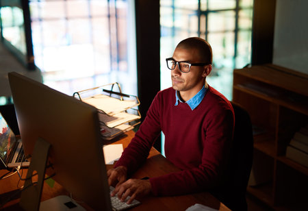 The deadline comes first. High angle shot of a handsome young man working late in his office.