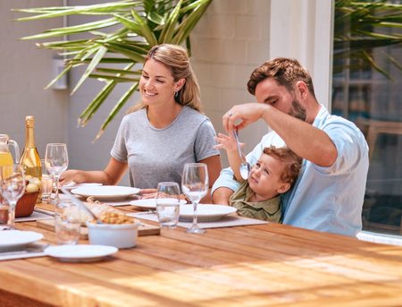 Food, mother and father with baby at table at an outdoor patio for holiday celebration with champagne and lunch in summer. Happy family, mom and dad with child fine dining together at home or houseの写真素材