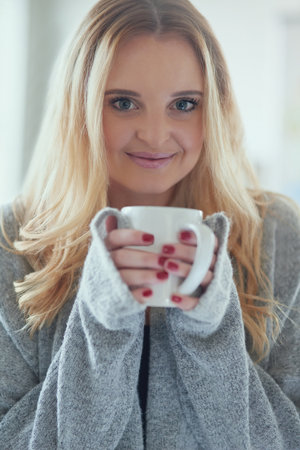 Coffee is my perfect kick-start. Portrait of an attractive young woman enjoying a cup of coffee at home.の写真素材