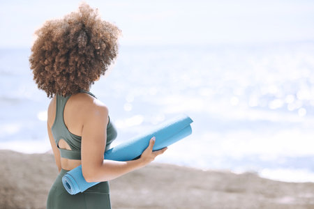 Black woman, yoga mat and enjoying ocean and view before zen, peaceful and relaxing exercise. A yogi and woman ready to meditate at beach. Nature, african american girl and meditation by seaの写真素材