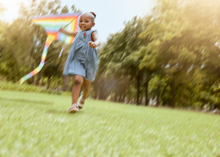 Girl, running with kite and nature park for happy, fun outdoor activity and freedom run in summer making childhood memory. Playful child, grass field and black kid playing outside on nature holidayの写真素材