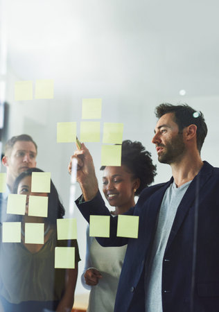 Coming up with a plan. a group of businesspeople working on a glass wall in the office.の写真素材