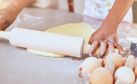 Child, baking and cooking with hands on table with rolling pin for pizza, pastry or cookie dough on messy kitchen counter with flour and eggs. Learning, hobby and girl learning skill to cook at, homeの写真素材