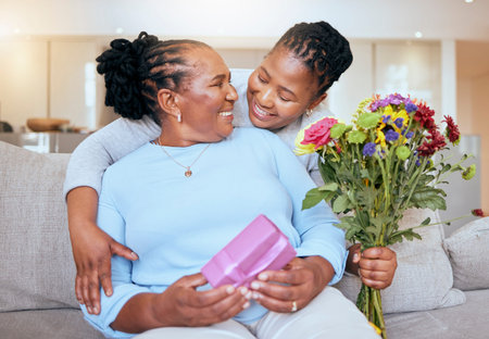 Black woman, mothers day and hug with flowers on sofa for love, box or gift to mom in home. Woman, bouquet and senior mama with wow, smile or happy for surprise, celebration or birthday on couchの写真素材