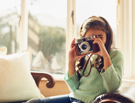 Shes got an eye for photography. a little girl taking pictures with a vintage camera at home.の写真素材