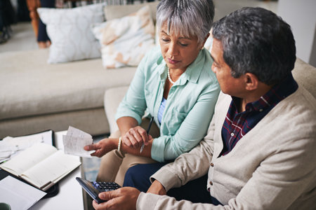 Going over the household expenses. an elderly couple working out a budget while sitting on the living room sofa.の写真素材