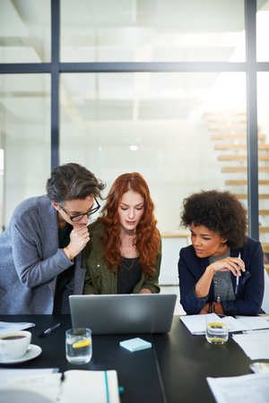 Getting everyone on the same page. three young creatives working together on a laptop in a modern office.の写真素材