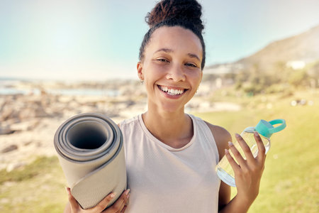 Nature, fitness and black woman with bottle and yoga mat ready to begin exercise, workout and training. Summer, yoga and portrait of young female with water exercising for health wellness by oceanの写真素材
