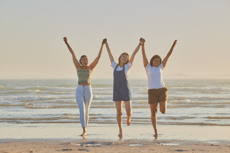 Holding hands, friends and women on beach, jump together and bonding or loving outdoor on summer vacation. Travel, young females or ladies enjoy seaside holiday, for girls trip and connect on break.の写真素材