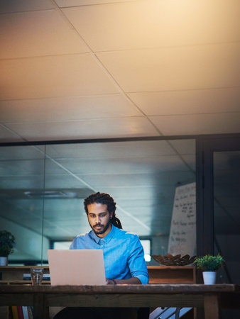 The extra hours can make all the difference. a young designer working late on a laptop in an office.
