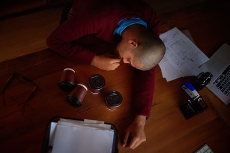 Even the coffee couldnt keep him awake. High angle shot of a young man asleep at his desk while...