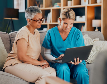 Home visit, woman and doctor with laptop on sofa checking medical results or chart online. Healthcare, technology and nurse or caregiver help consulting with patient on computer on living room couch.の写真素材