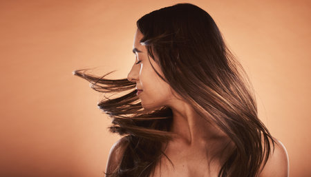 Hair care, beauty and woman with care for body against a brown mockup studio background. Cosmetic, content and young girl model flipping her perfect, soft and healthy hair with mock up spaceの写真素材