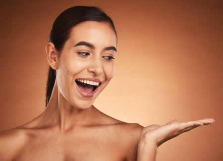 Skincare, wow and hand of woman for marketing, advertising and happy against a brown mockup studio background. Spa, cosmetics and model with surprise in wellness and makeup and mock up spaceの写真素材